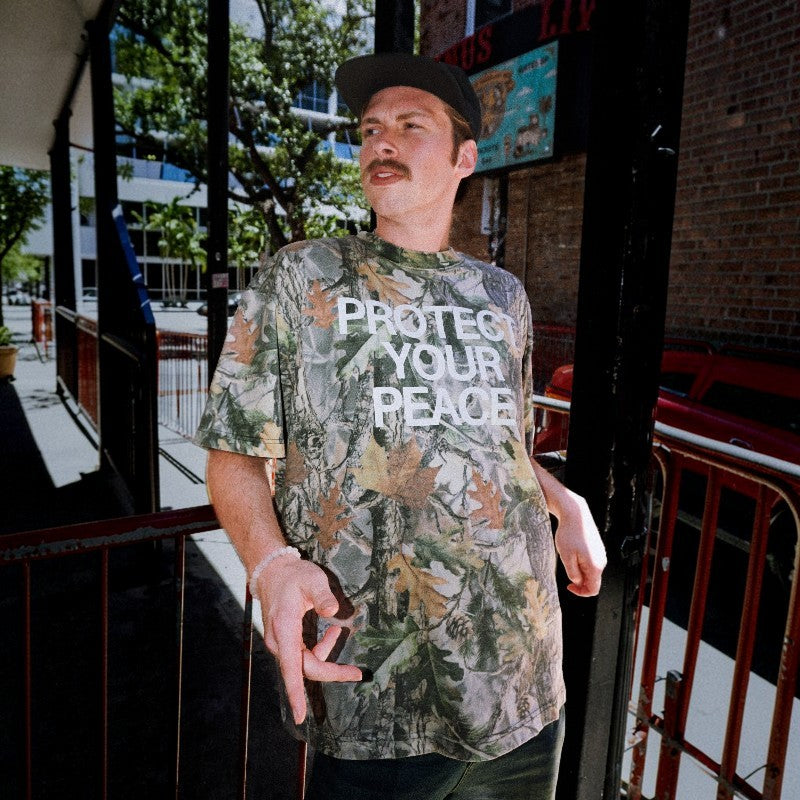Model wearing Comfortable Silence At All Costs camouflage oversized box tee with Protect Your Peace graphic