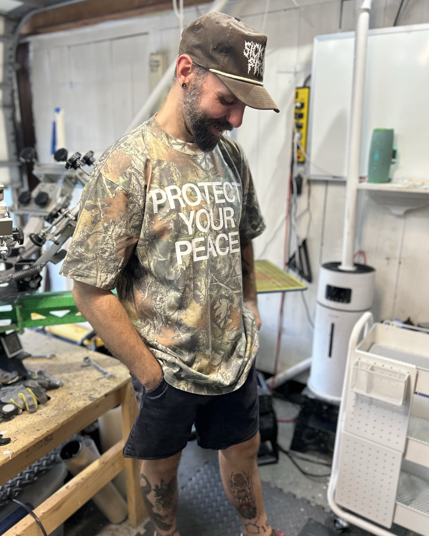 Man wearing a camouflage t-shirt with text in a workshop setting