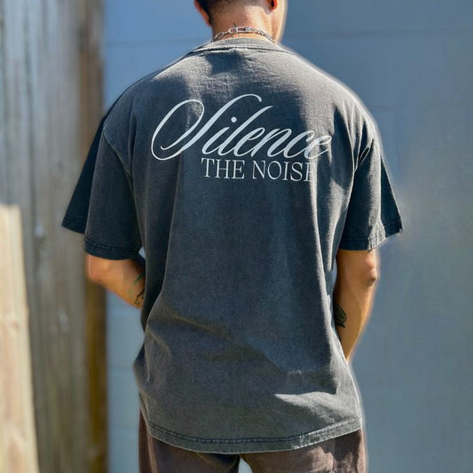 Person wearing a black t-shirt with the words Silence the Noise on the back, standing against a wooden and blue wall.