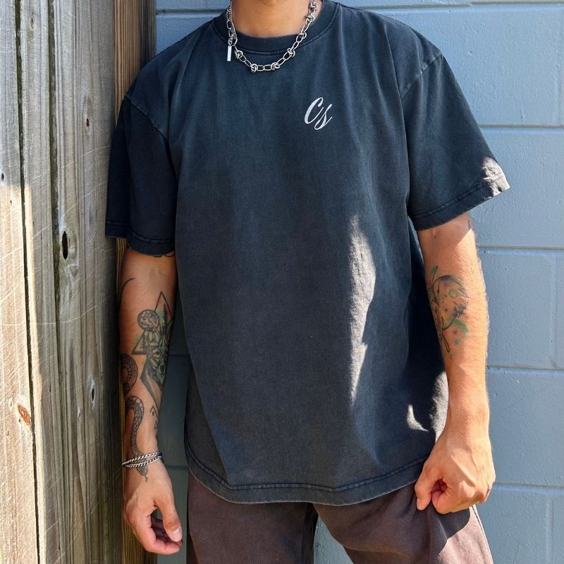 Person wearing a black t-shirt with a logo, standing against a wooden and blue wall.