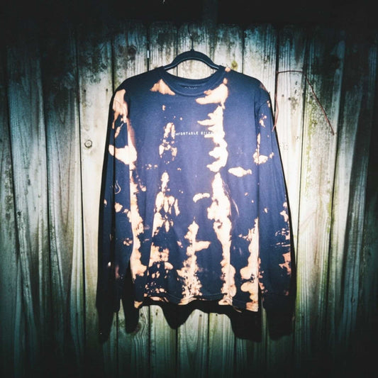Black long-sleeve shirt with bleached pattern on a hanger against a wooden fence.
