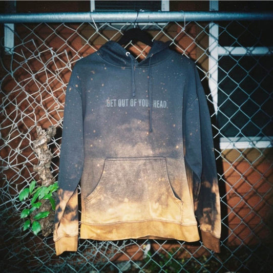 Bleached hoodie with text 'GET OUT OF YOUR HEAD' hanging against a chain-link fence.