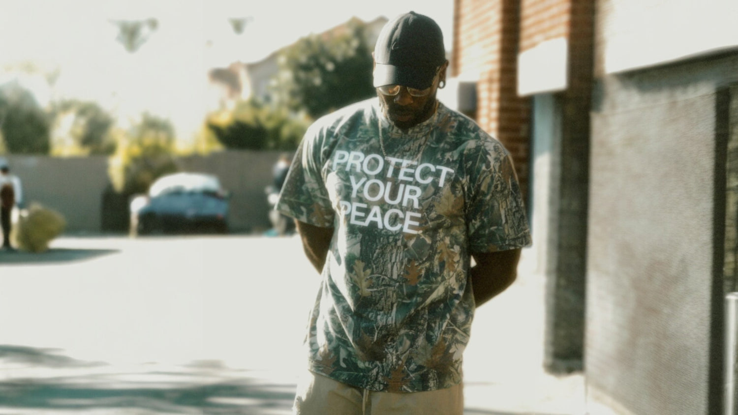 Man wearing a camouflage t-shirt with 'Protect Your Peace' text outdoors.