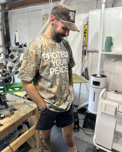 Man wearing a camouflage t-shirt with text in a workshop setting
