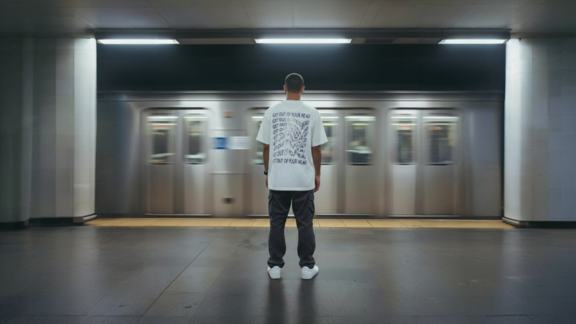 Person standing in a subway station with a blurred train in the background