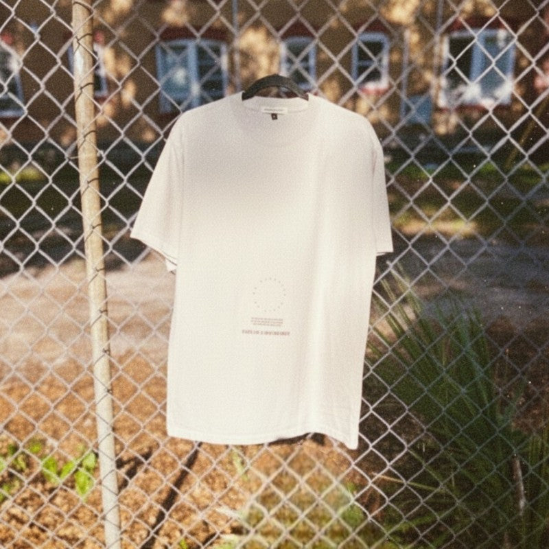 "No Darkness No Light" oversized tee in faded bone with small center graphic on a chain link fence.