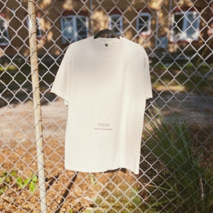 "No Darkness No Light" oversized tee in faded bone with small center graphic on a chain link fence.