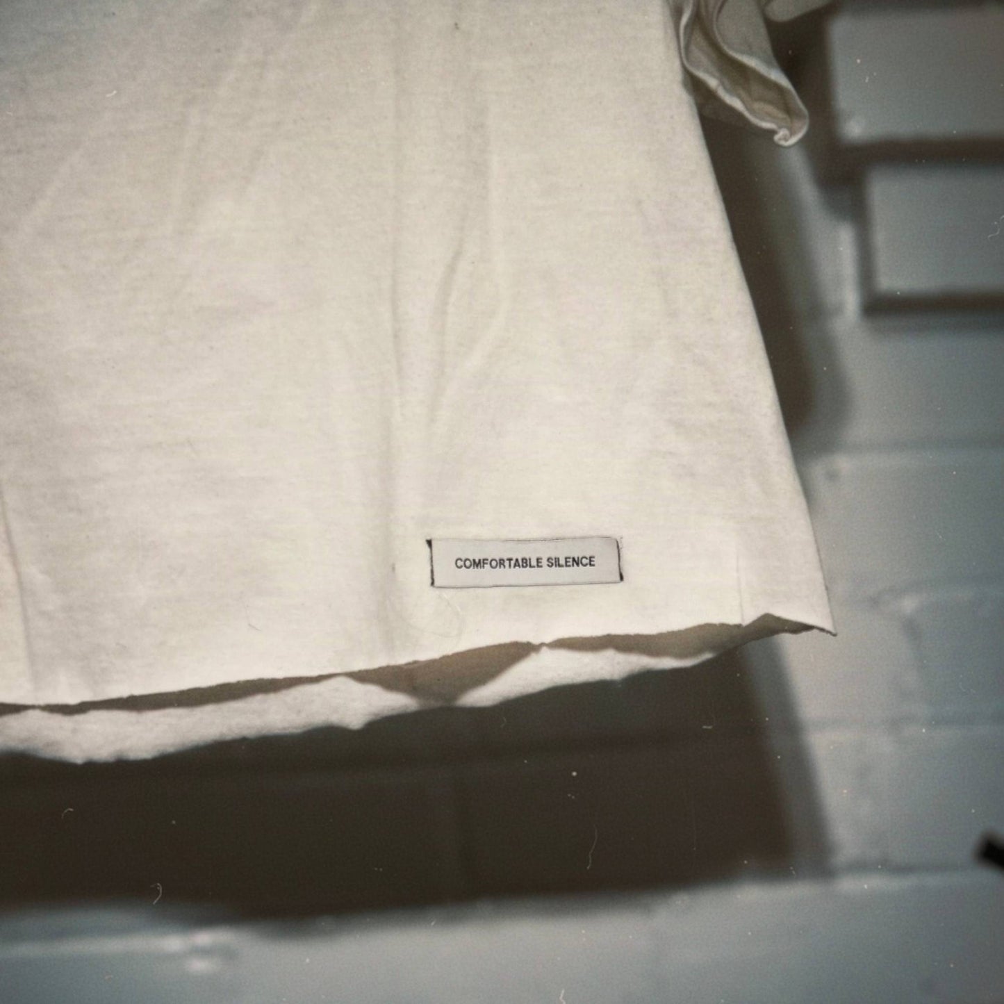 A close-up of a premium woven label reading 'COMFORTABLE SILENCE' on a white t-shirt.