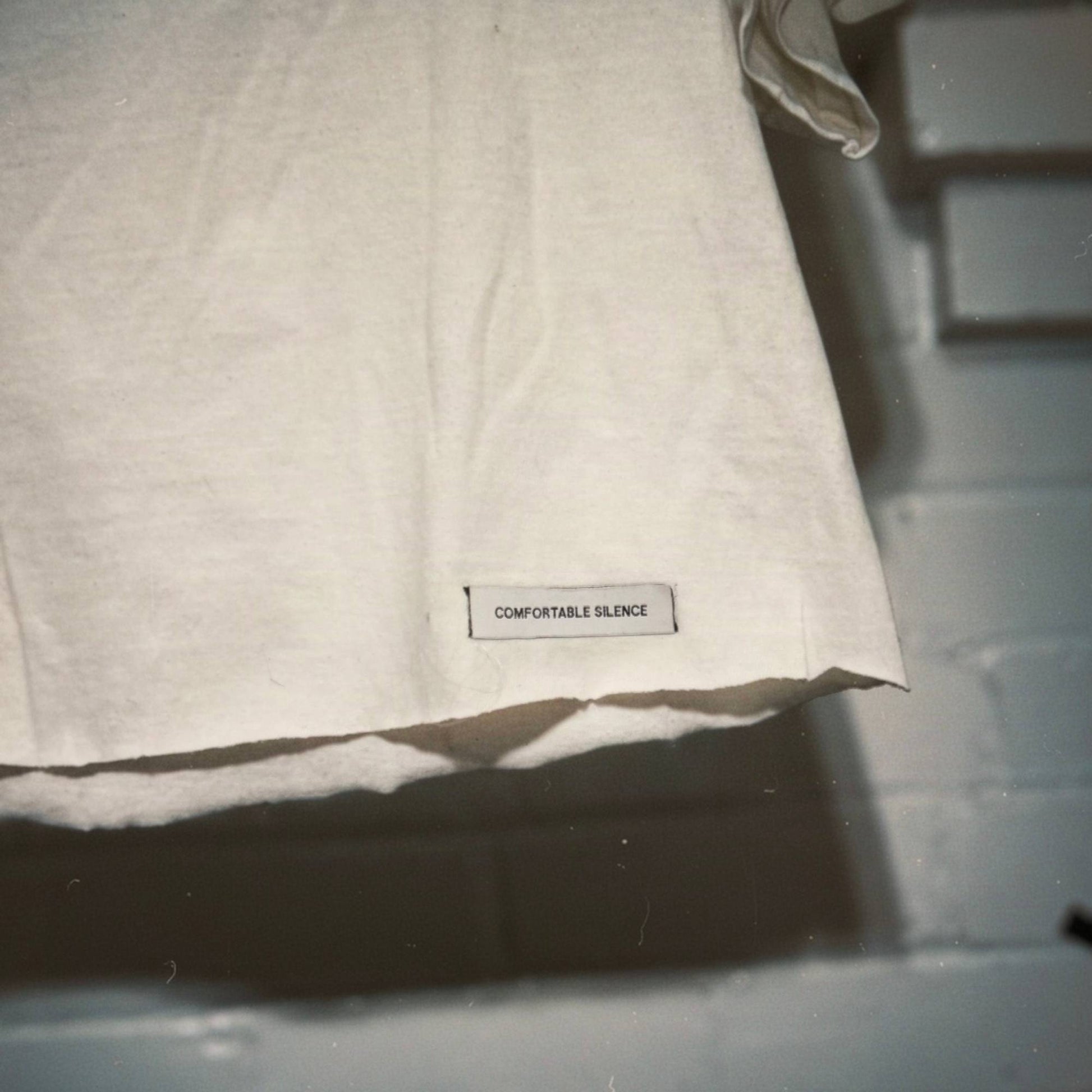 A close-up of a premium woven label reading 'COMFORTABLE SILENCE' on a white t-shirt.