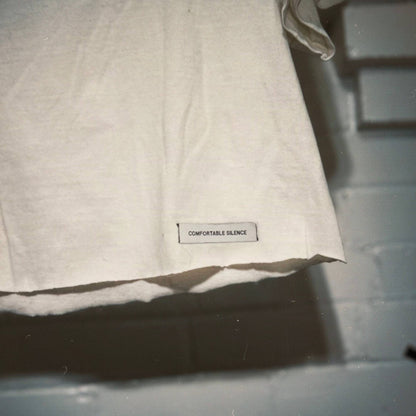 A close-up of a premium woven label reading 'COMFORTABLE SILENCE' on a white t-shirt.