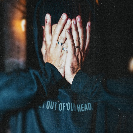 Person wearing a hoodie with text on the back, hands covering face.