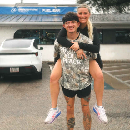 Matt Johnson and his wife; Matt wearing the At All Costs Camo Oversized Tee by Comfortable Silence.