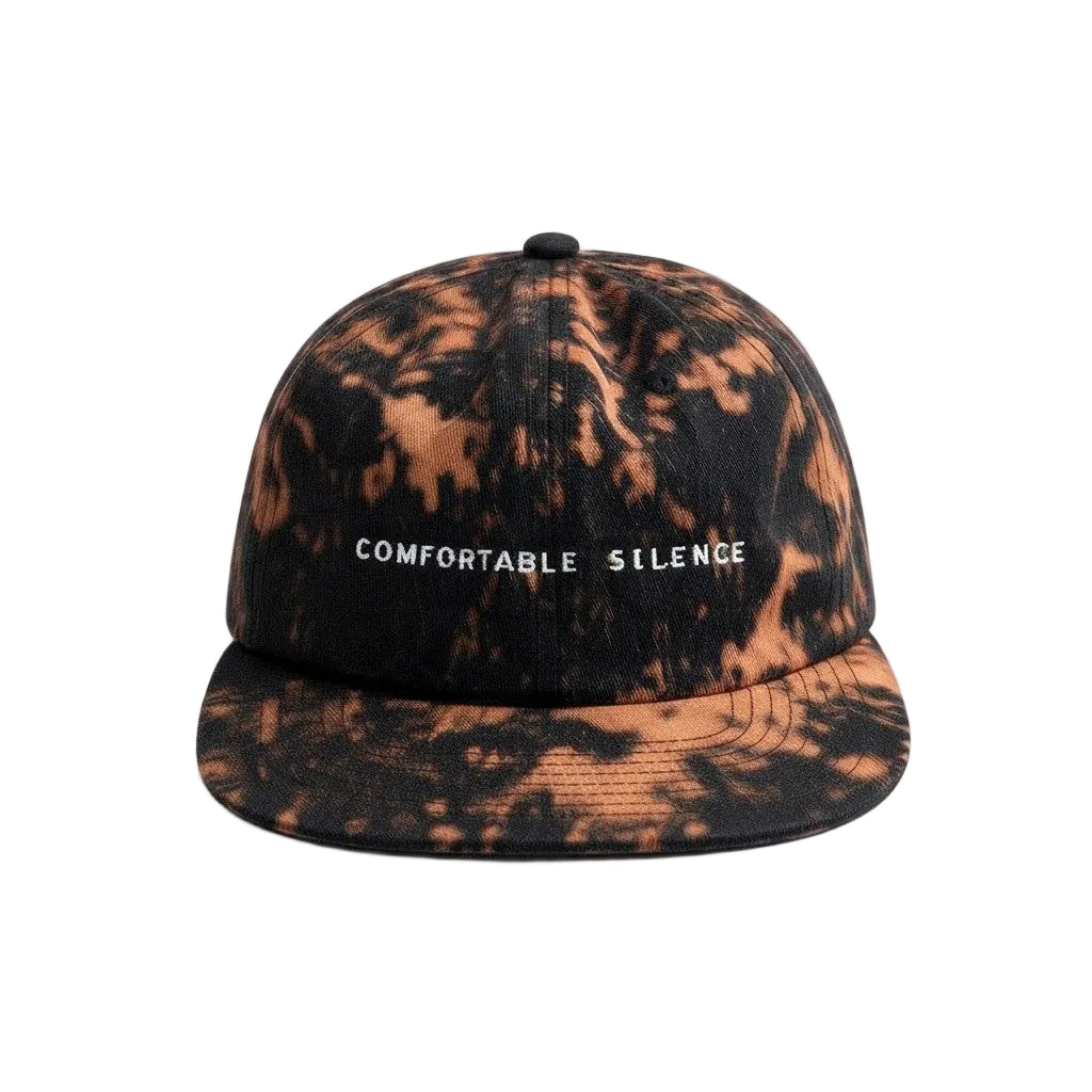 A flat-brim baseball cap with a black and copper-brown tie-dye pattern, featuring the text 'COMFORTABLE SILENCE' embroidered in white on the front.